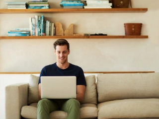 Mann sitzt auf dem Sofa mit offenem Laptop